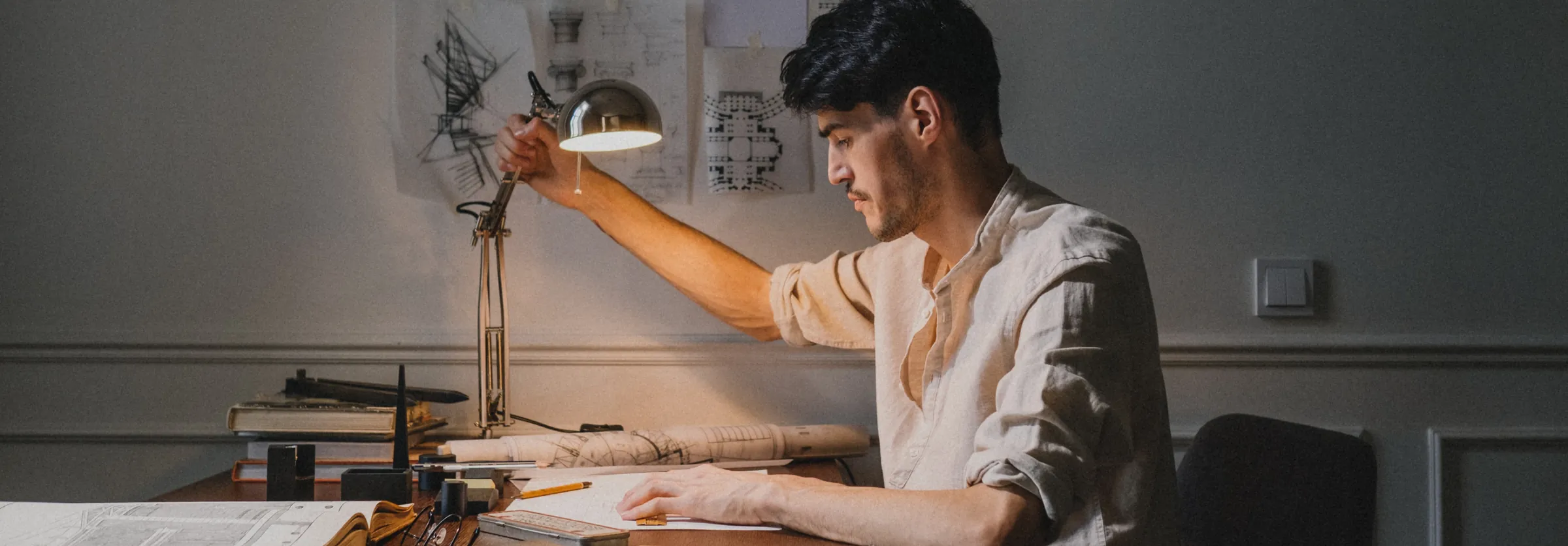 A founder working alone at a drafting desk under a lamp